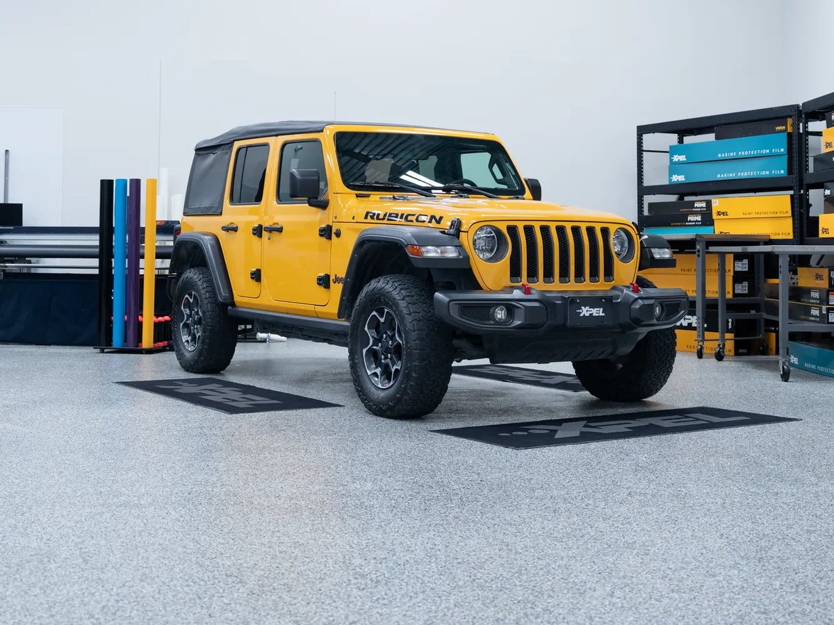 Yellow Jeep Rubicon in the XPEL installation bay with XPEL film racks