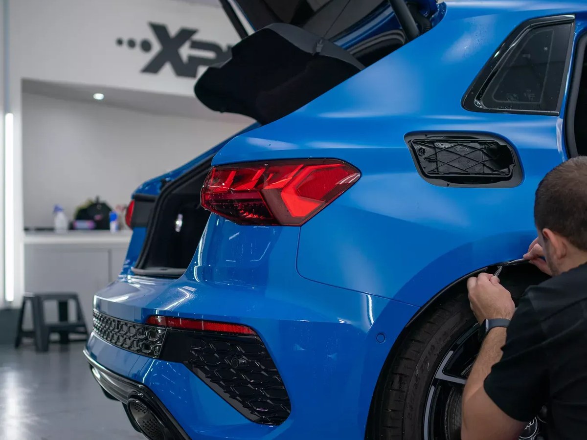 Installer fitting paint protection film around the rear wheel arch of a blue Audi