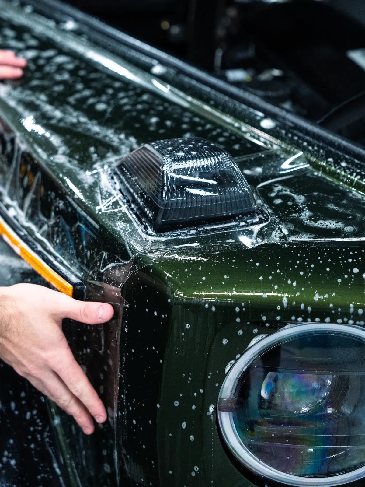 XPEL Ultimate Plus clear paint protection film being installed on a green car hood